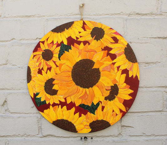 round canvas with acrylic painted sunflowers on with brown background hanging on grey brick wall