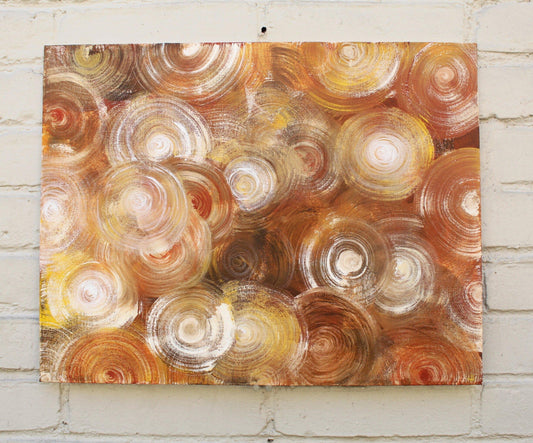 brown abstract painting with gold and white spirals on grey brick wall