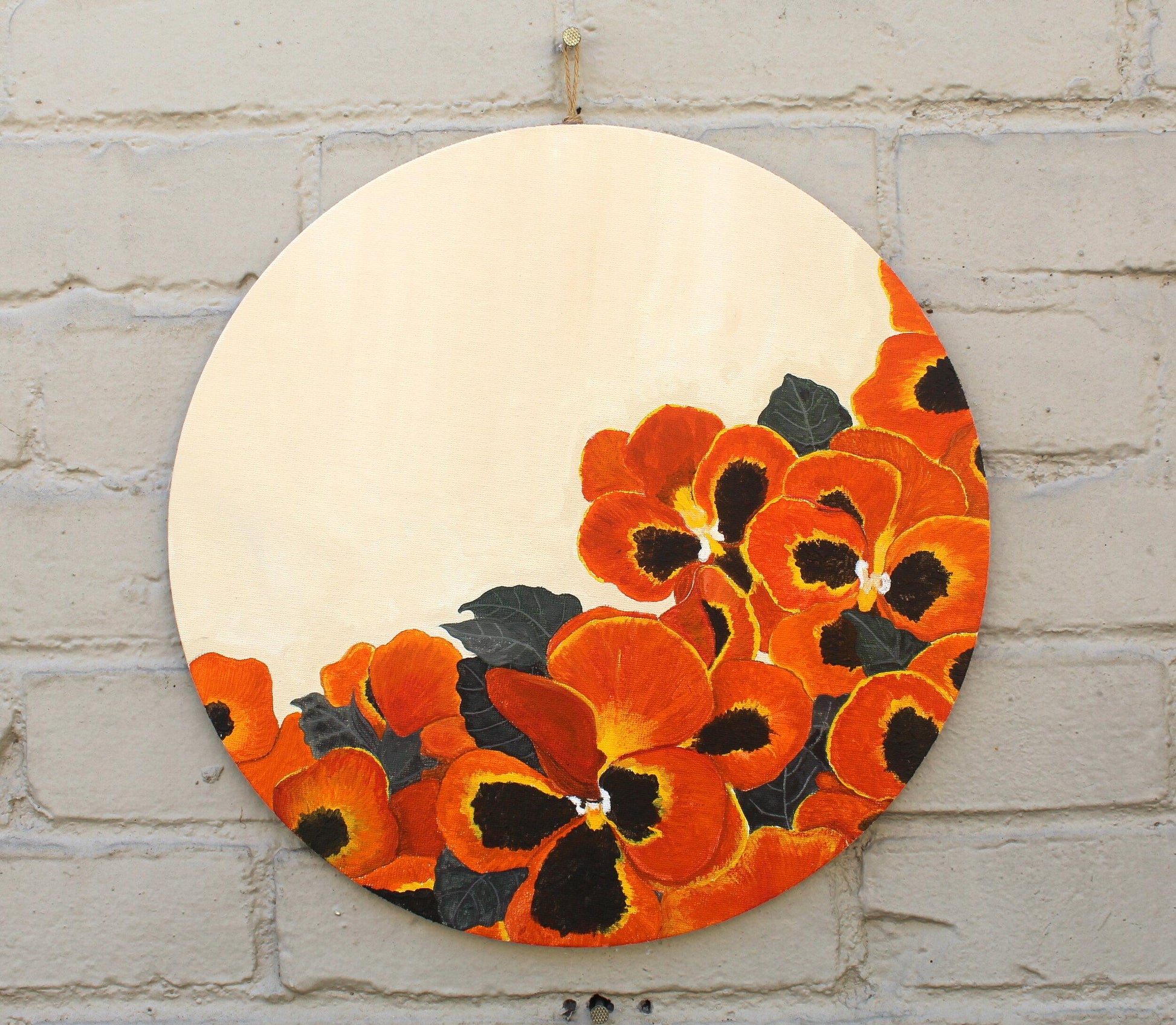 Painting of pansy flowers that are all orange, yellow, and black hanging on grey brick wall