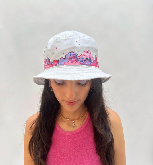 front view of white bucket hat painted with pink and purple clouds 