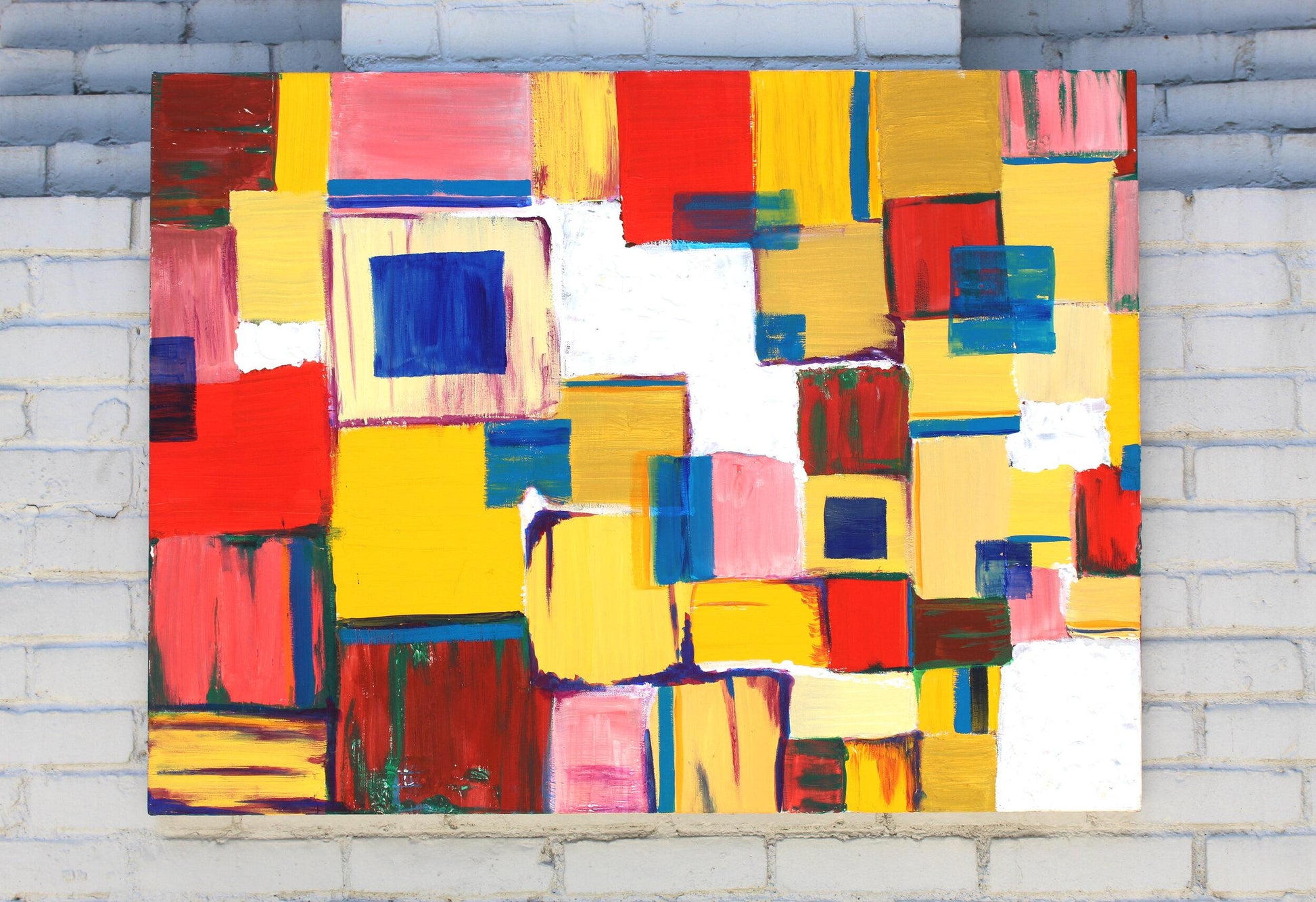 abstract painting of squares in red, yellow, pink, and blue tones hanging on grey brick wall