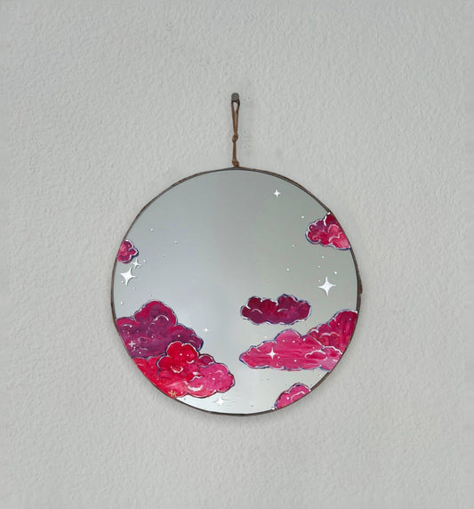 Round mirror painted with pink skies and white stars on white wall 