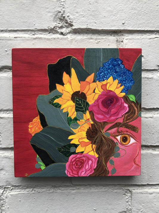 half of woman's face with brown hair surrounded by pink roses, sunflowers, blue hydrangeas, and leaves on a hot pink background on grey brick wall