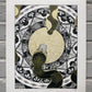 two black, white, and gold snakes meeting at center of page on top of circular gold pattern and black and white shapes on grey brick wall