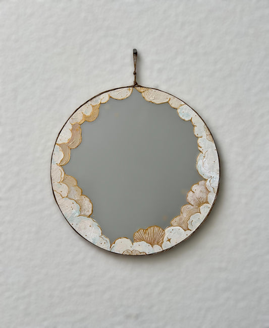 round mirror painted with white and cream clouds hanging on white wall