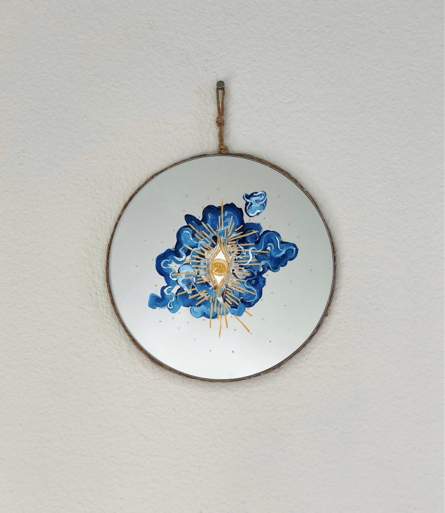 round mirror. abstract blue and white cloud in center with gold eye and rays on top on white wall