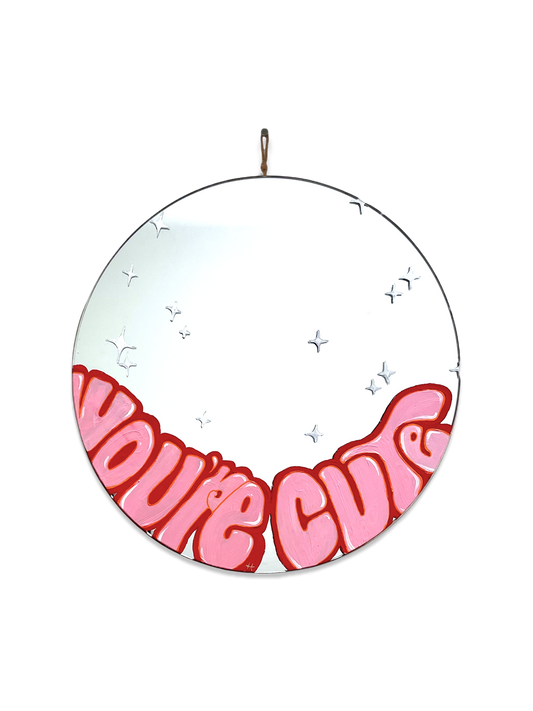 round mirror with light pink writing on the bottom and outlined in red. White sparkles on the mirror.